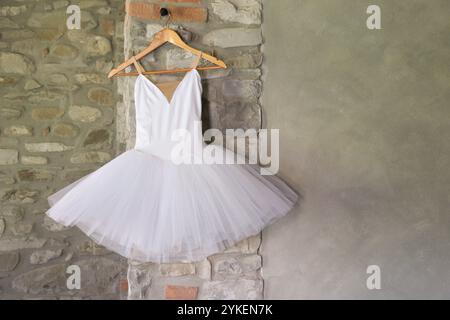 tutu de ballet blanc accroché sur cintre en bois, fond de mur en pierre grise Banque D'Images