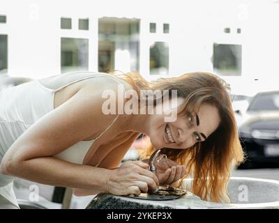 Femme joyeuse buvant dans une fontaine publique Banque D'Images