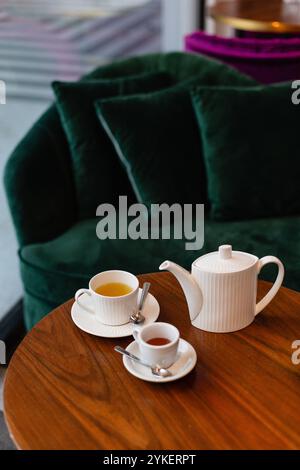 Service à thé au miel sur une table en bois arrondie et un canapé vert Banque D'Images