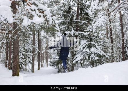 Vue arrière jeune femme courant vers les arbres enneigés dans les chutes de neige Banque D'Images