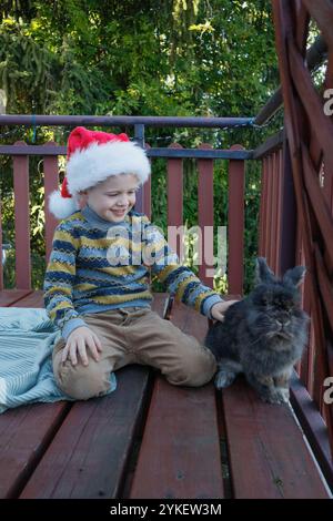 Garçon jouant avec le lapin en chapeau de Père Noël sur la terrasse Banque D'Images