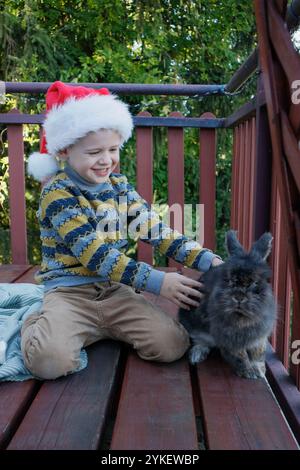 Garçon jouant avec le lapin en chapeau de Père Noël sur la terrasse Banque D'Images