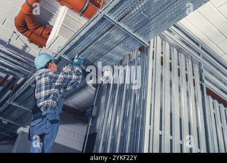 Un travailleur de la construction se concentre sur l'installation d'une ossature métallique au-dessus, assurant la stabilité structurelle dans un nouveau bâtiment. L'environnement est industriel A. Banque D'Images