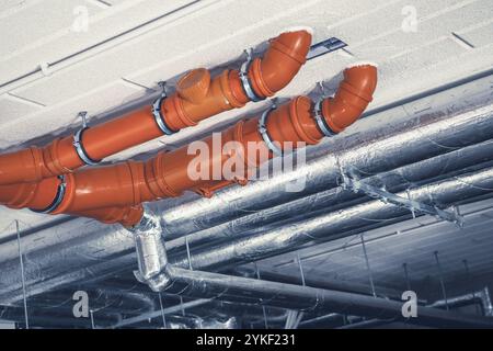 Des tuyaux orange vif longent le plafond d'un bâtiment commercial, entourés de conduits métalliques, mettant en valeur l'infrastructure de la construction moderne Banque D'Images