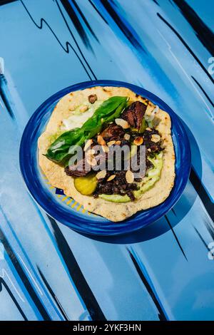 Une présentation gourmande de tortilla aux joues de veau garnie d'amandes et de basilic frais sur une assiette bleue éclatante, renforçant son attrait visuel. Banque D'Images