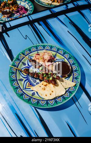 Une image vibrante de coeurs de poulet yakitori accompagné de salade de radis et de pain plat, présenté sur une assiette joliment dessinée à côté d'une piscine, enhanc Banque D'Images
