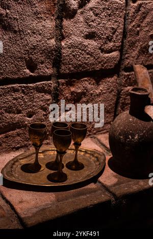 Une image d'ambiance mettant en valeur l'équipement de vinification géorgien traditionnel, avec des verres à vin complexes et une carafe en argile rustique, serrée contre un textu Banque D'Images