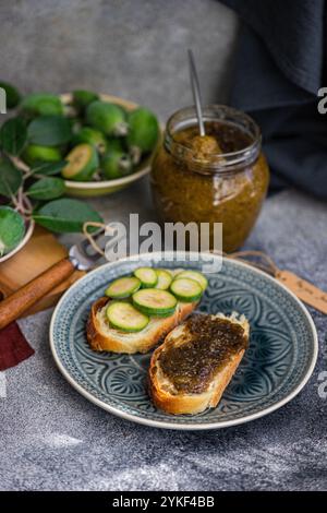 Régalez-vous dans un thé floral avec des sandwichs croustillants avec de la confiture de feijoa fraîche, accompagnés de fruits feijoa mûrs, parfaits pour une collation rafraîchissante Banque D'Images