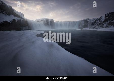 Enveloppée dans la neige, une cascade islandaise impressionnante cascades sous un ciel brumeux la scène tranquille capture la sérénité et la beauté brute de l'Islande Banque D'Images