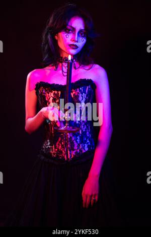 Une femme gothique se tient debout dans un cadre faiblement éclairé, tenant une bougie elle porte un corset en dentelle noire et un maquillage sombre, évoquant une atmosphère mystérieuse et éthérée Banque D'Images