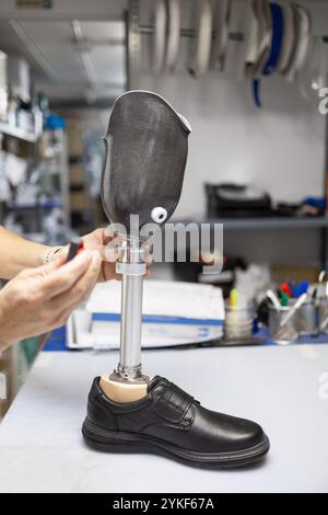 Gros plan des mains d'un technicien ajustant une jambe prothétique la jambe est équipée d'une chaussure formelle, placée dans un magasin de fournitures orthopédiques envir Banque D'Images