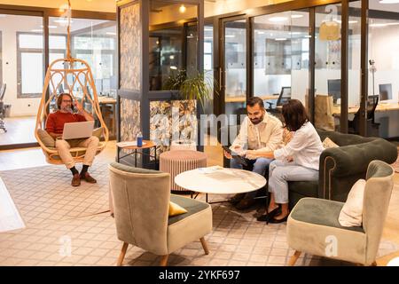 Professionnels travaillant en collaboration dans un espace de coworking élégant la zone dispose de sièges confortables, une chaise pivotante et un décor moderne, favorisant un produc Banque D'Images