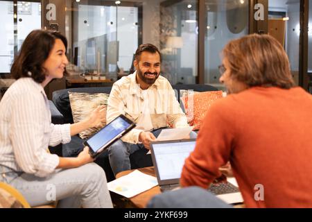 Un groupe de professionnels engagés dans une discussion animée dans un espace de coworking confortable plein de lumière naturelle les ordinateurs portables et les tablettes sont utilisés comme collaboratifs Banque D'Images