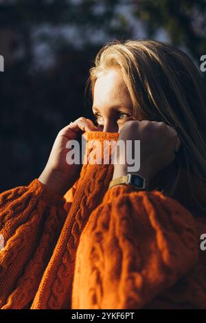 Une femme profite d'un moment de tranquillité, enveloppée dans un pull orange tricoté confortable les teintes chaudes et la texture douce transmettent un sentiment de confort et de paix, Banque D'Images