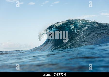 Une vague océanique captivante capturée à mi-crête sous un ciel bleu clair L'image met en évidence la puissance brute et la beauté de la mer, évoquant la tranquillité et un Banque D'Images