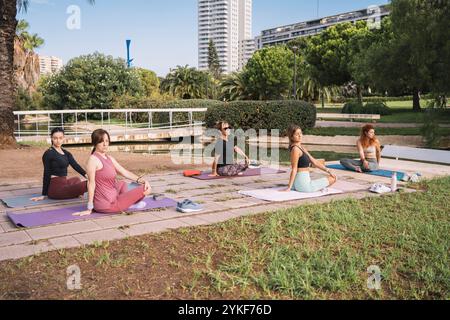 Groupe diversifié de femmes pratiquant le yoga dans un cadre paisible de parc de la ville. Ils effectuent diverses poses, sous la direction d'une femme instructrice de yoga, fos Banque D'Images