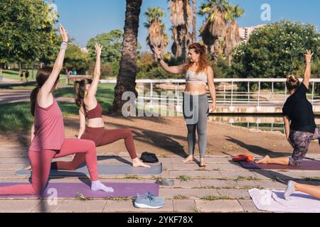 Une femme instructrice de yoga guide un groupe de femmes à travers diverses poses de yoga dans un cadre paisible de parc extérieur. L'instructeur et les participants sont en AC Banque D'Images