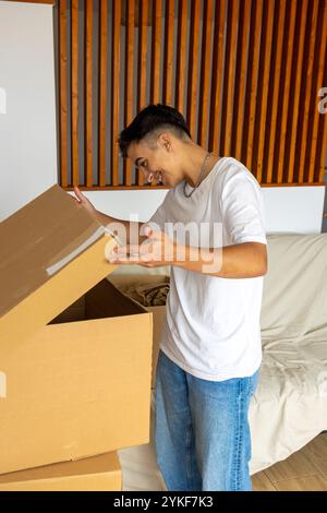 Un jeune homme trans, souriant alors qu'il déballait des boîtes dans son nouvel appartement lumineux, symbolisant un nouveau départ et la fierté de son identité Banque D'Images