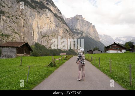 Dans le cadre pittoresque de Lauterbrunnen, en Suisse, une femme se tient sur un chemin rural, contemplant les majestueuses falaises qui l’entourent Banque D'Images