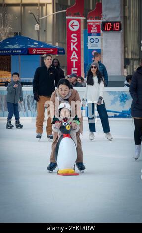 Patineurs mères et enfants sur glace à la patinoire du Bryant Park Winter Village 2024. Dans Midtown Manhattan près de la 42ème rue. L'enfant utilise une aide de patin pingouin Banque D'Images