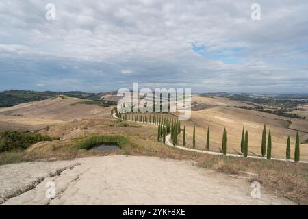 Vue imprenable sur la campagne toscane sereine en Italie présentant des collines ondulantes, des champs cultivés et des lignes emblématiques de cyprès sous un nuage Banque D'Images