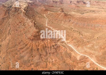 Vue d'en haut, cette image aérienne capture une vue imprenable sur le vaste désert de l'Utah. Un sentier sinueux et poussiéreux serpente à travers le te texturé et orange Banque D'Images