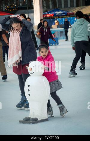 Patineurs sur glace mère et fille à la patinoire Bryant Park Winter Village 2024. Dans Midtown Manhattan près de la 42ème rue. La fille utilise un bonhomme de neige pour patins Banque D'Images