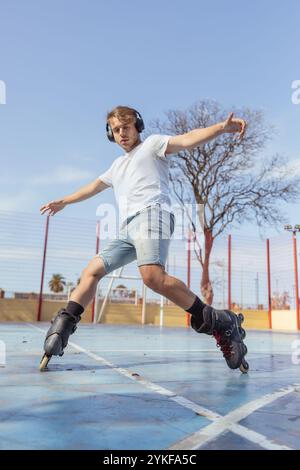 D'en bas, le jeune homme est capturé en mouvement alors qu'il roule en douceur sur un court coloré dans un parc urbain, portant des écouteurs et maintenant BA Banque D'Images