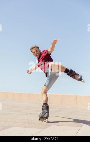 Un jeune homme avec enthousiasme roller dans un espace extérieur ensoleillé, effectuant une manœuvre de patinage habile avec une position dynamique, vêtu d'une tenue décontractée Banque D'Images