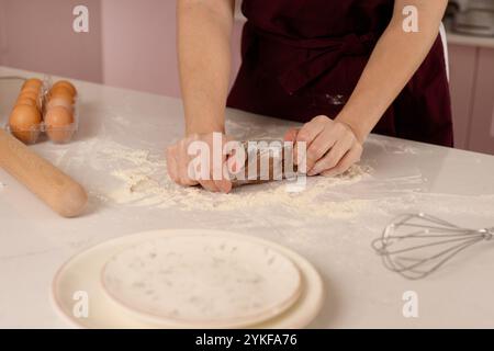 Une personne pétrit méticuleusement la pâte brune dans une cuisine bien équipée, entourée d'œufs et d'ustensiles de cuisson Banque D'Images