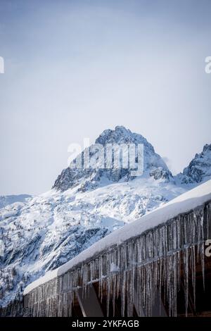 Un magnifique paysage hivernal dans les Alpes, avec un sommet de montagne enneigé contre un ciel clair des glaçons pendent d'un toit en bois, ajoutant à la Ser Banque D'Images