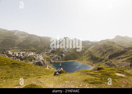 Une scène sereine dans les Asturies, en Espagne, avec un randonneur surplombant un magnifique lac de montagne entouré de pics verdoyants sous un ciel clair Banque D'Images