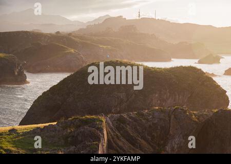 Le coucher de soleil captivant jette des teintes dorées sur la côte accidentée des Asturies, avec un sentier isolé serpentant le long des falaises spectaculaires et de l'océan serein Banque D'Images