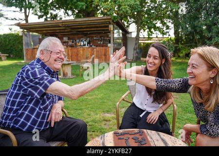 Un moment joyeux capture une famille caucasienne générationnelle diversifiée engagée dans un jeu de société en plein air. Un homme âgé et deux femmes, une jeune Adu Banque D'Images