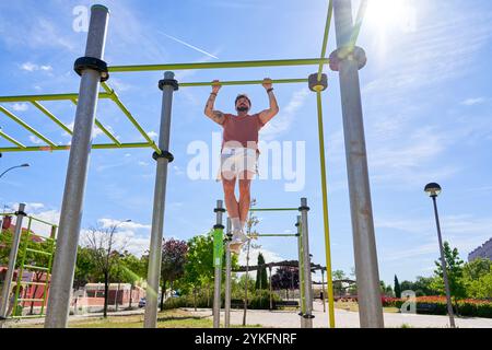 Un jeune athlète effectue des tractions dans un parc de calisthenics en plein air, faisant preuve de force et de dévouement dans un cadre d'entraînement naturel en plein air. Banque D'Images