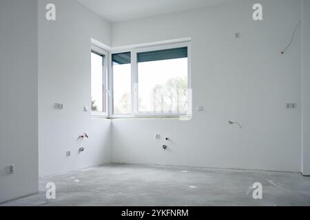 Spacieux appartement vide en cours de rénovation avec grande fenêtre, sol en béton et murs blancs. Nouveau bâtiment en construction Banque D'Images