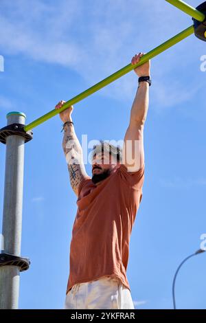 Un jeune athlète effectue des tractions dans un parc de calisthenics en plein air, faisant preuve de force et de dévouement dans un cadre d'entraînement naturel en plein air. Banque D'Images