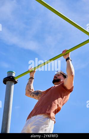 Un jeune athlète effectue des tractions dans un parc de calisthenics en plein air, faisant preuve de force et de dévouement dans un cadre d'entraînement naturel en plein air. Banque D'Images