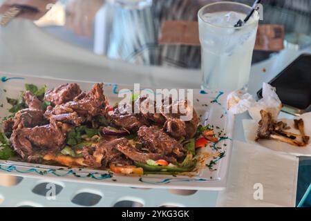 La viande d'Iguaçu, une spécialité locale de Curaçao, est servie dans une assiette avec des légumes. Les os restants sont sur une serviette. Spécialité de Curaçao : ragoût d'iguane au restaurant Blue View Sunset Terrace, Westpunt, Curaçao, Kòrsou Banque D'Images