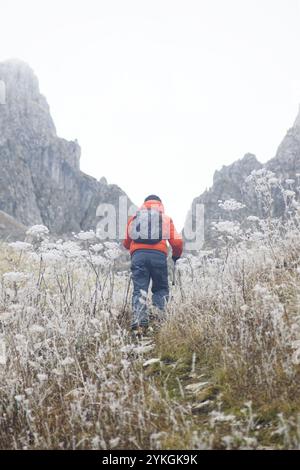 Un homme marche le long d'un sentier de montagne par une journée froide : un touriste avec un sac à dos sur fond de belles montagnes et de plantes couvertes de gel. Banque D'Images