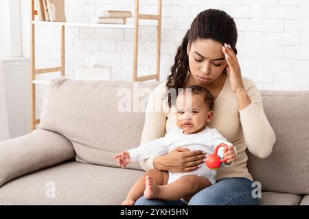 Maman noire ayant mal de tête assis avec bébé en pleurs à la maison Banque D'Images