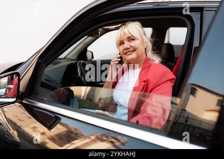 Une femme dans une veste rouge sourit en parlant au téléphone dans une voiture Banque D'Images