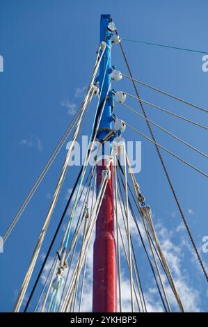 Un mât de bateau vibrant avec diverses cordes et gréement placé contre un ciel bleu clair, évoquant l'aventure maritime et la liberté. Banque D'Images