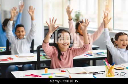 Divers petits écoliers levant les mains en classe Banque D'Images