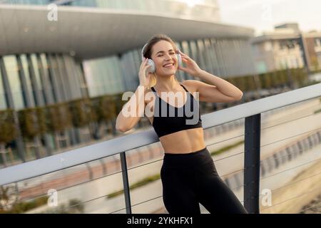 Une femme joyeuse en vêtements d'action jogging le long de la rivière, portant des écouteurs et savourant le soleil du matin. Son sourire reflète son amour pour le fitness et en Banque D'Images