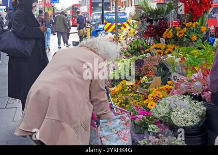 Femme plus âgée avec un chariot d'achat de fleurs à l'étal de fleurs devant la station de métro Brixton High Street octobre 2024 Londres Angleterre Royaume-Uni KATHY DEWITT Banque D'Images