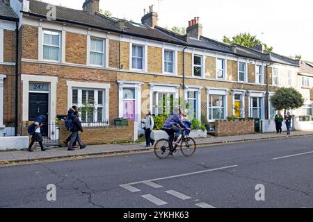 Les gens marchant devant la rangée de maisons mitoyennes à l'extérieur sur Railton Road dans le quartier de Brixton octobre 2024 Londres Angleterre Royaume-Uni KATHY DEWITT Banque D'Images