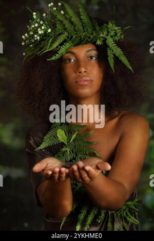 Portrait d'une belle jeune femme noire tenant une plante verte dans les paumes de ses mains Banque D'Images