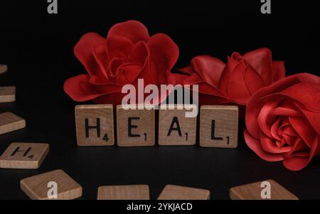 Trois roses rouges derrière des lettres en bois scrabble avec le mot HEAL. Concept de la Journée mondiale contre le cancer. Journée mondiale de la santé mentale. Journée mondiale de la santé Banque D'Images