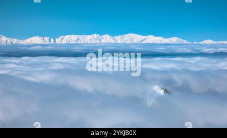 Montagnes couvertes de neige déchiquetées émergeant à travers une épaisse couche de nuages Banque D'Images